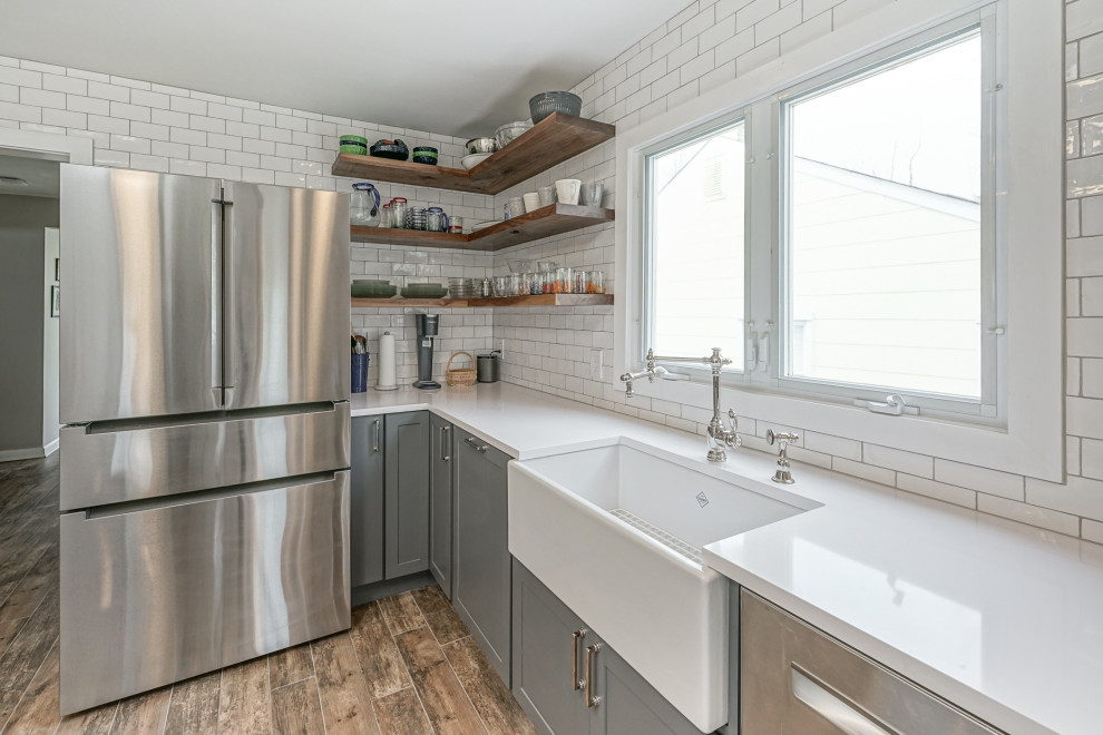 Large transitional l-shaped eat-in kitchen in Philadelphia with an undermount sink, shaker cabinets, grey cabinets, concrete benchtops, white splashback, subway tile splashback, stainless steel appliances, light hardwood floors, no island, multi-coloured floor and white benchtop.