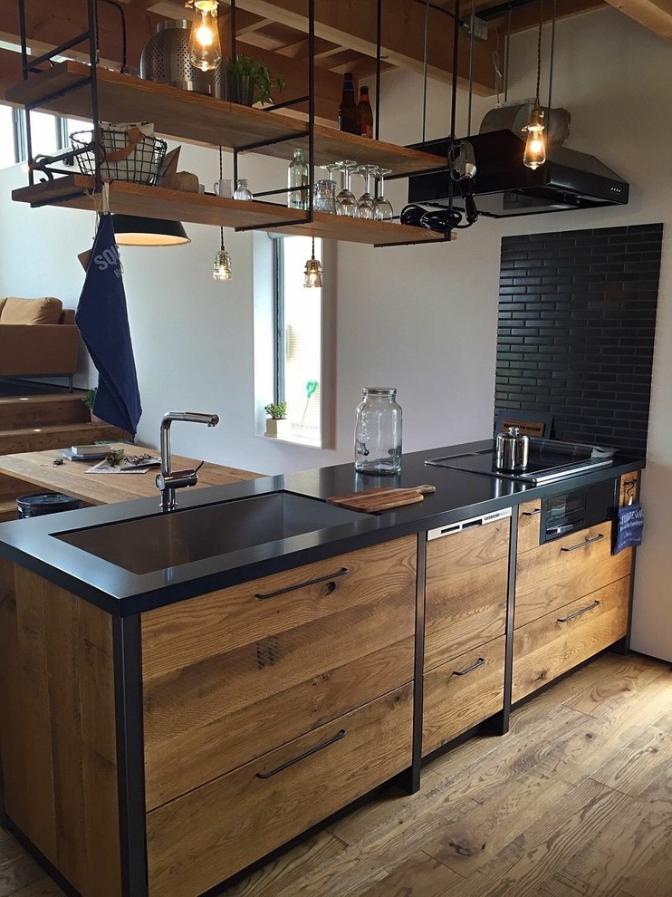 Industrial single-wall open plan kitchen in Other with a single-bowl sink, flat-panel cabinets, medium wood cabinets, medium hardwood floors, a peninsula, brown floor and black benchtop.