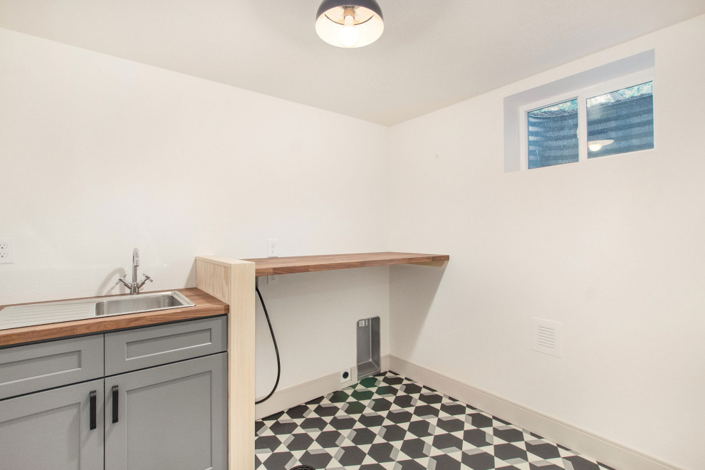 Inspiration for a small midcentury single-wall dedicated laundry room in Denver with an utility sink, shaker cabinets, grey cabinets, wood benchtops, white walls, vinyl floors, a side-by-side washer and dryer, multi-coloured floor and brown benchtop.