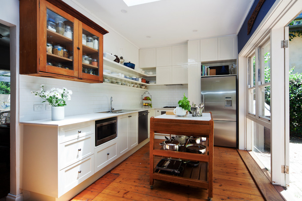 This is an example of a mid-sized country l-shaped eat-in kitchen in Sydney with shaker cabinets, white splashback, ceramic splashback, stainless steel appliances, medium hardwood floors and with island.