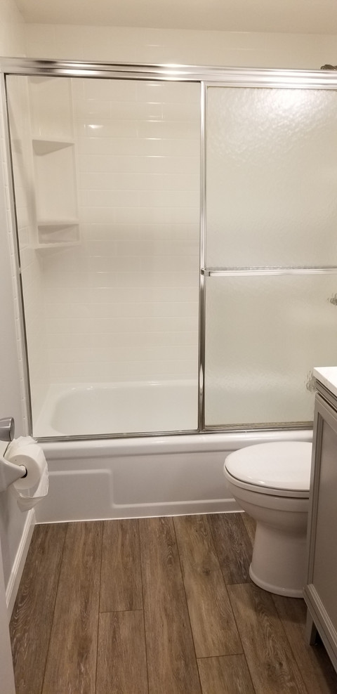 Photo of a mid-sized contemporary bathroom in Miami with recessed-panel cabinets, grey cabinets, white tile, grey walls, laminate floors, brown floor and white benchtops.