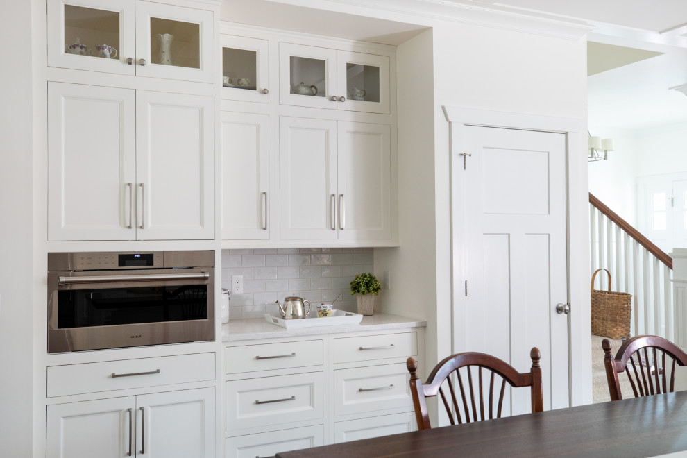 Inredning av ett klassiskt stort vit vitt kök, med en undermonterad diskho, luckor med infälld panel, vita skåp, bänkskiva i kvarts, vitt stänkskydd, stänkskydd i mosaik, rostfria vitvaror, mörkt trägolv och en köksö