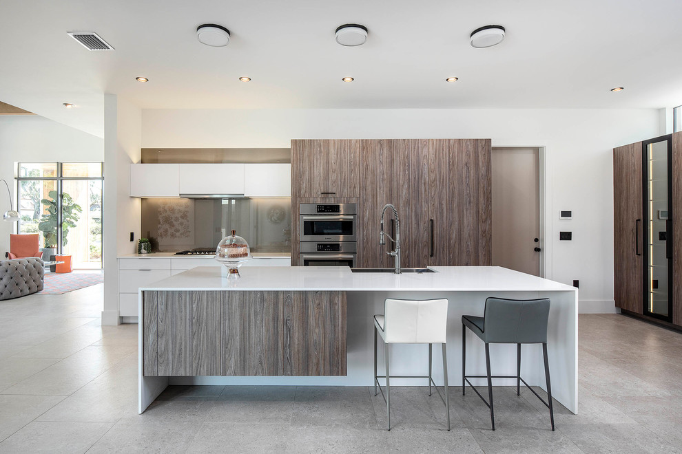Photo of a contemporary open plan kitchen in Orlando with a farmhouse sink, flat-panel cabinets, quartz benchtops, glass sheet splashback, stainless steel appliances, with island, white benchtop, white cabinets, grey splashback and grey floor.