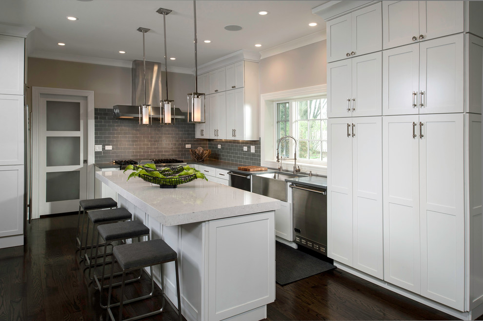 Inspiration for a transitional kitchen in Chicago with a farmhouse sink, shaker cabinets, white cabinets, quartz benchtops, grey splashback, glass tile splashback, stainless steel appliances, dark hardwood floors and with island.