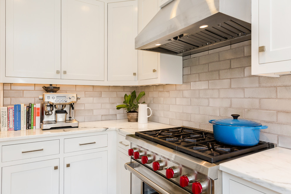 Mid-sized transitional l-shaped eat-in kitchen in Boston with an undermount sink, shaker cabinets, white cabinets, marble benchtops, grey splashback, cement tile splashback, stainless steel appliances, dark hardwood floors, a peninsula, brown floor and white benchtop.