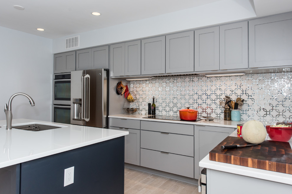 This is an example of a mid-sized transitional l-shaped eat-in kitchen in DC Metro with an undermount sink, shaker cabinets, blue cabinets, glass benchtops, grey splashback, mosaic tile splashback, stainless steel appliances, porcelain floors and with island.