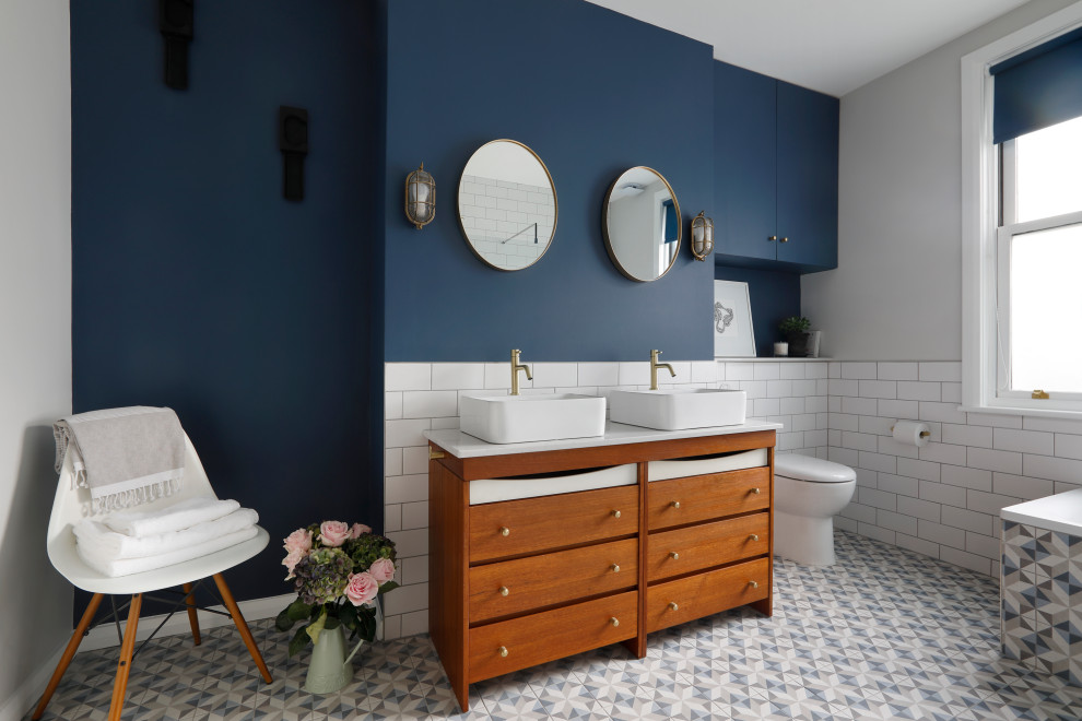 Inspiration for a large contemporary master bathroom in Sussex with medium wood cabinets, a corner tub, an open shower, a one-piece toilet, white tile, ceramic tile, blue walls, porcelain floors, a vessel sink, engineered quartz benchtops, blue floor, an open shower, white benchtops, a double vanity, a freestanding vanity and flat-panel cabinets.