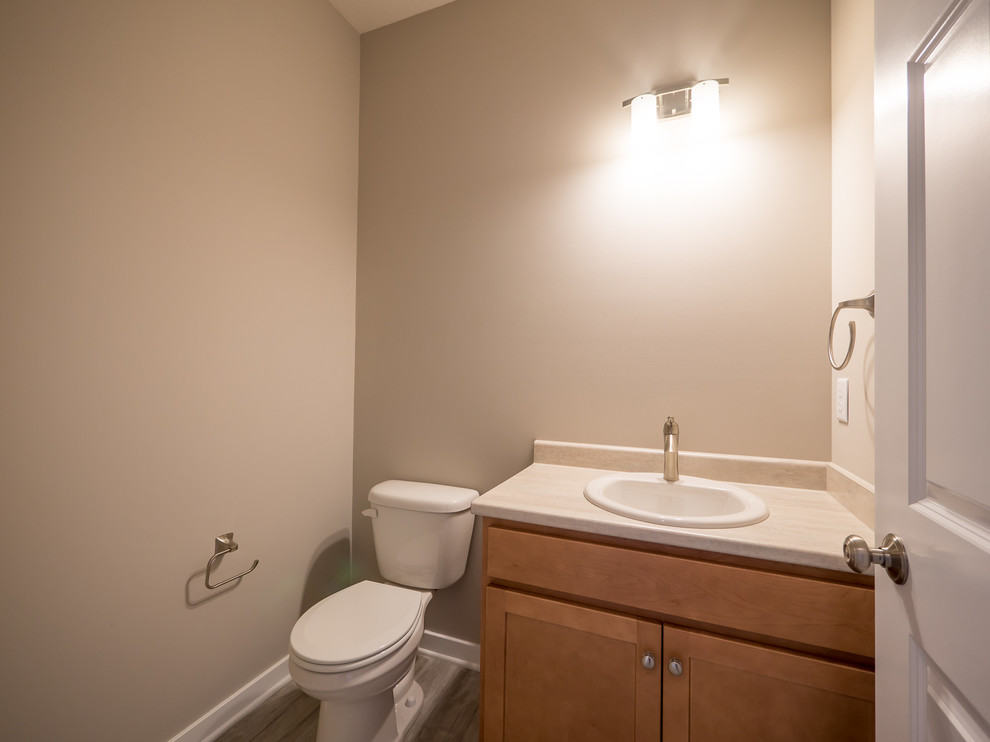 Photo of a mid-sized arts and crafts powder room in Other with flat-panel cabinets, light wood cabinets, a two-piece toilet, beige tile, beige walls, vinyl floors, a drop-in sink and laminate benchtops.