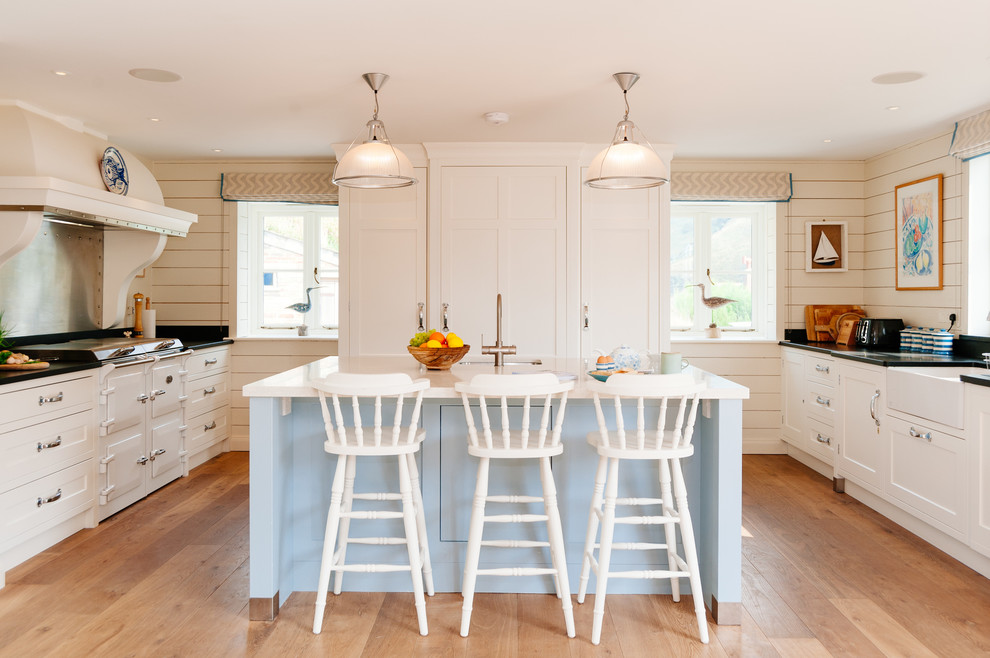 Photo of a beach style u-shaped kitchen in Cornwall with a farmhouse sink, shaker cabinets, white cabinets, panelled appliances, medium hardwood floors and with island.