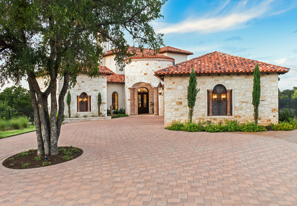 Expansive mediterranean three-storey beige house exterior in Austin with stone veneer, a gable roof and a tile roof.