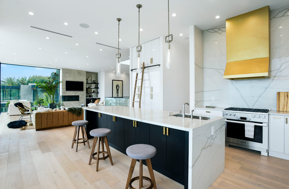 Inspiration for a large contemporary kitchen in Los Angeles with flat-panel cabinets, white cabinets, white splashback, stainless steel appliances, light hardwood floors, with island and white benchtop.