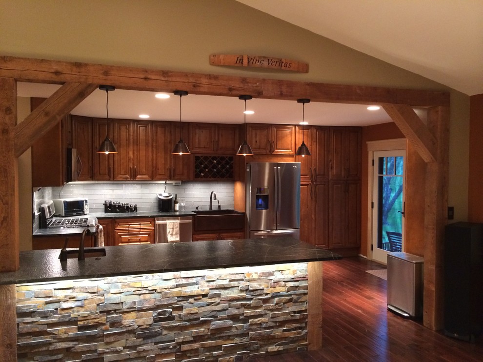 Large mountain style l-shaped medium tone wood floor eat-in kitchen photo in St Louis with a farmhouse sink, raised-panel cabinets, granite countertops, gray backsplash, glass tile backsplash, stainless steel appliances and a peninsula