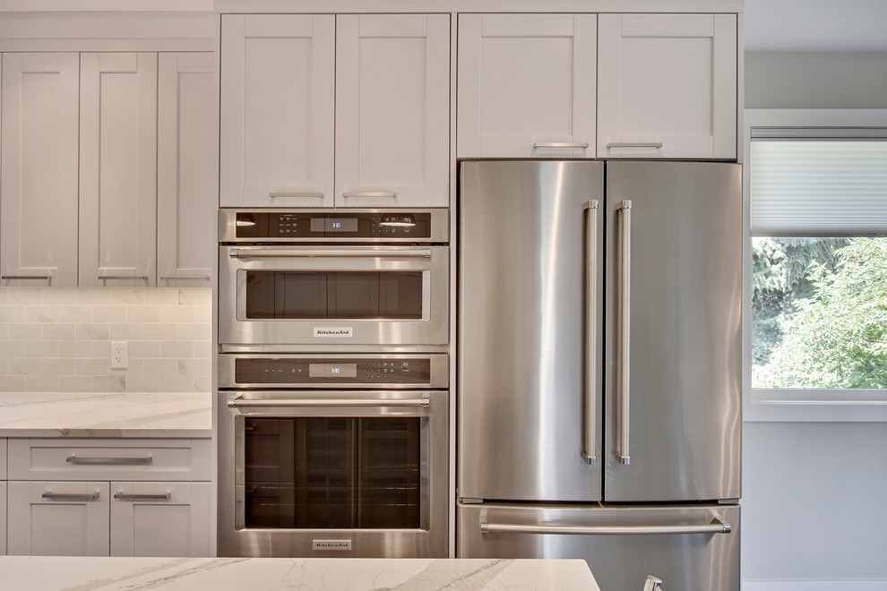 Eat-in kitchen - transitional l-shaped medium tone wood floor eat-in kitchen idea in Calgary with an undermount sink, shaker cabinets, white cabinets, quartz countertops, white backsplash, porcelain backsplash, stainless steel appliances and an island