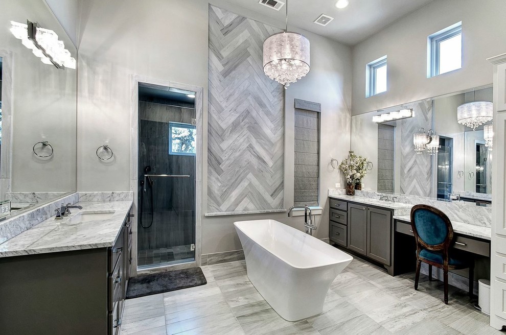 Photo of a large transitional master bathroom in Austin with an undermount sink, shaker cabinets, grey cabinets, marble benchtops, a freestanding tub, gray tile, stone tile, grey walls, marble floors, a corner shower, grey floor and a hinged shower door.