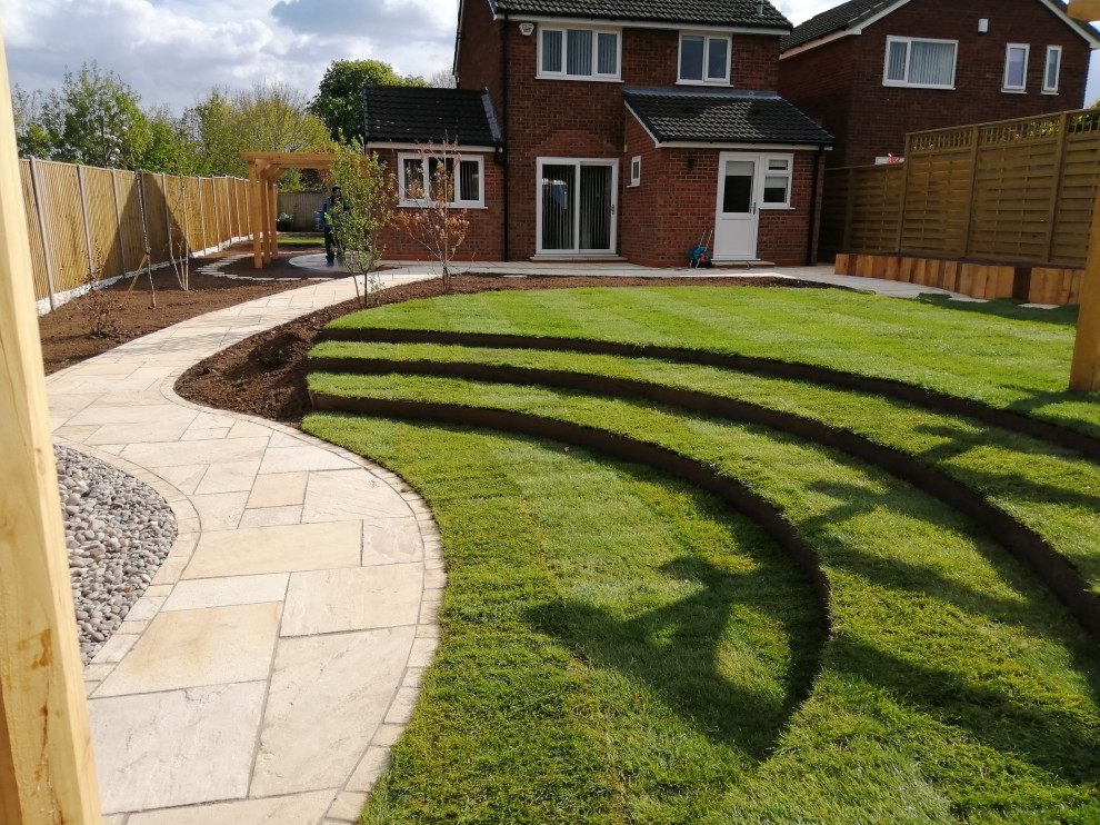 Photo of a mid-sized country backyard full sun formal garden for summer in West Midlands with with lawn edging, natural stone pavers and a wood fence.
