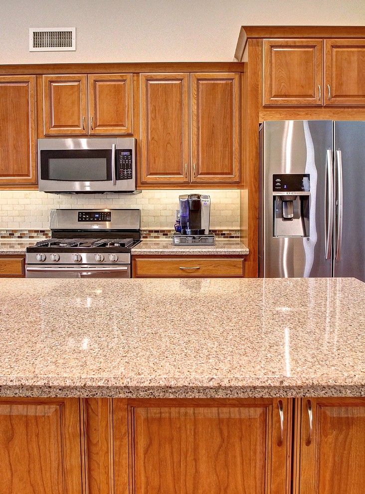 Eat-in kitchen - mid-sized l-shaped medium tone wood floor eat-in kitchen idea in Phoenix with a farmhouse sink, raised-panel cabinets, medium tone wood cabinets, beige backsplash, stone tile backsplash, stainless steel appliances and an island