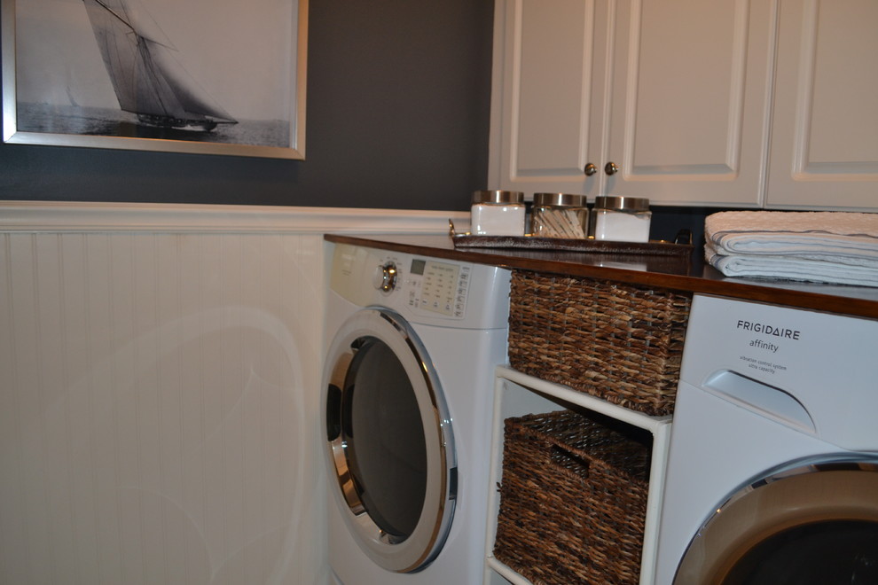 Photo of a mid-sized beach style galley dedicated laundry room in Nashville with flat-panel cabinets, white cabinets, wood benchtops, blue walls, limestone floors, a side-by-side washer and dryer, white floor and brown benchtop.