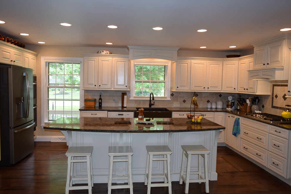 Inspiration for a transitional medium tone wood floor and brown floor kitchen remodel with a farmhouse sink, raised-panel cabinets, white cabinets, quartz countertops, beige backsplash, ceramic backsplash, black appliances and an island