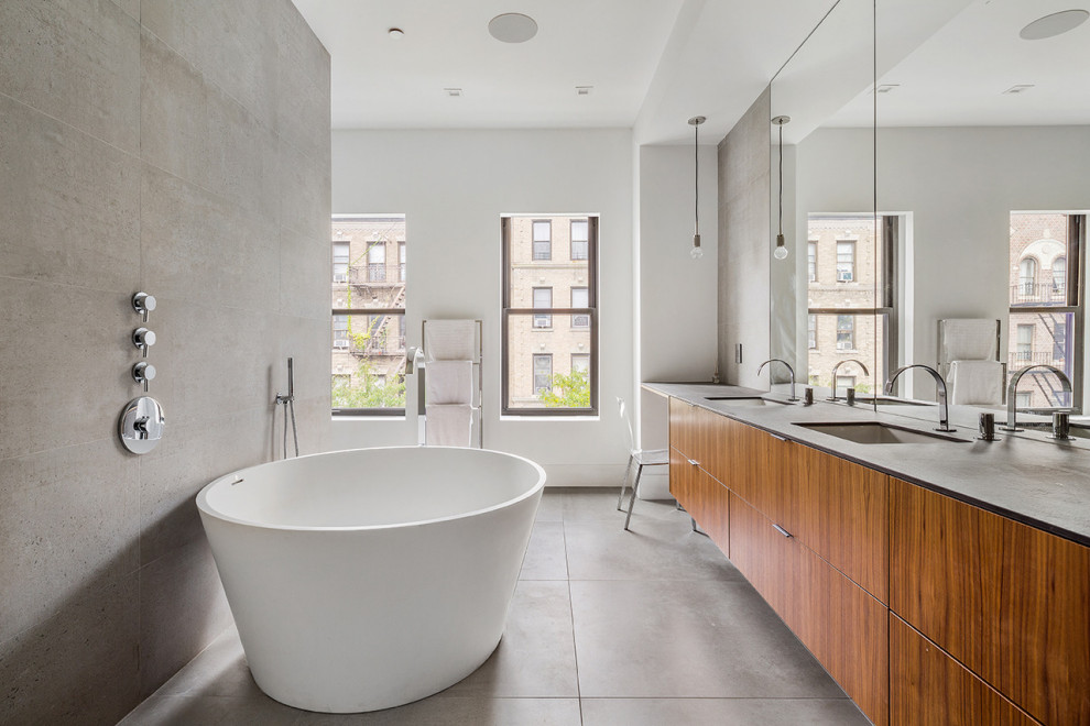 This is an example of an expansive contemporary master bathroom in New York with flat-panel cabinets, medium wood cabinets, a freestanding tub, a curbless shower, a wall-mount toilet, gray tile, porcelain tile, white walls, porcelain floors, an integrated sink, solid surface benchtops, grey floor, a hinged shower door, grey benchtops, a shower seat, a double vanity and a floating vanity.