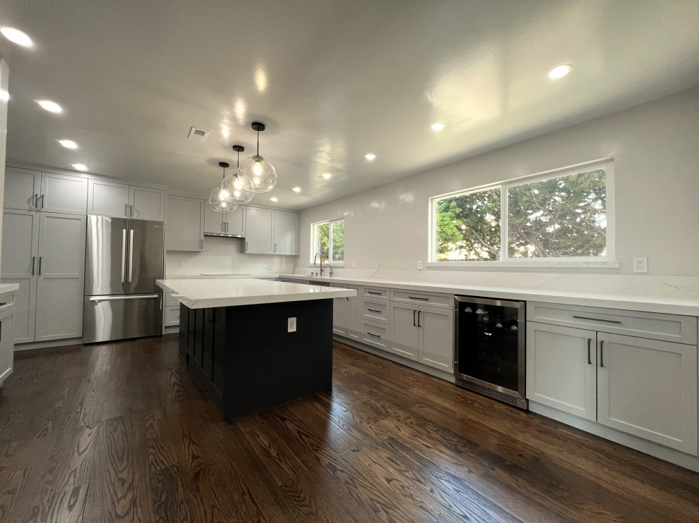 Exempel på ett avskilt, stort modernt vit vitt l-kök, med en undermonterad diskho, skåp i shakerstil, grå skåp, bänkskiva i kvarts, vitt stänkskydd, rostfria vitvaror, mörkt trägolv, en köksö och brunt golv