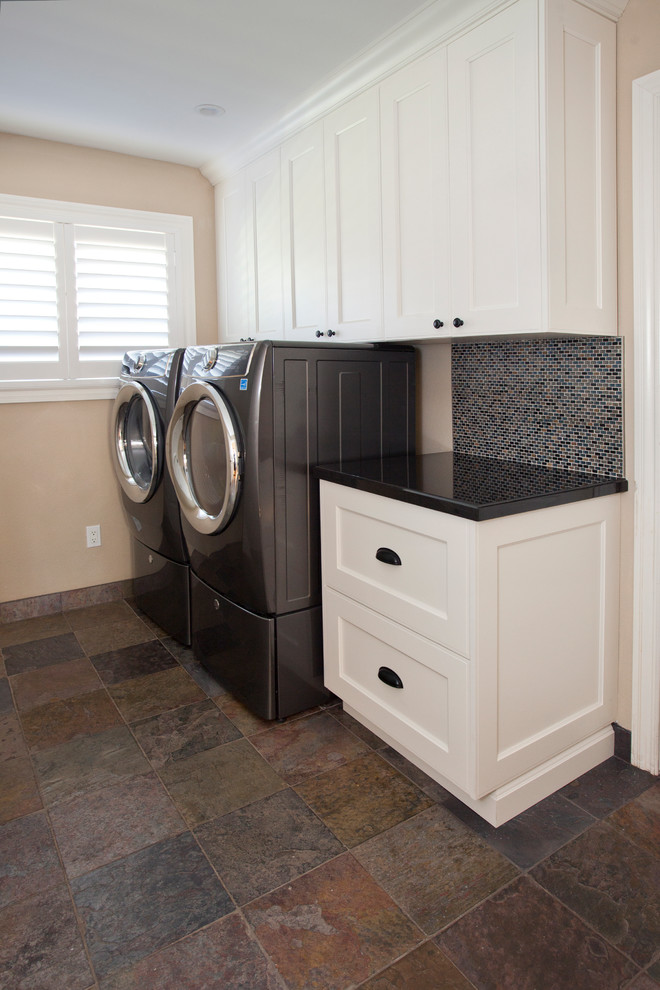 Photo of a mid-sized transitional single-wall dedicated laundry room in San Francisco with shaker cabinets, white cabinets, granite benchtops, beige walls, slate floors, a side-by-side washer and dryer and multi-coloured floor.