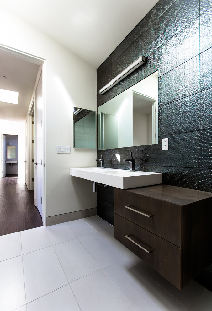 Photo of a mid-sized modern 3/4 bathroom in San Diego with a vessel sink, flat-panel cabinets, dark wood cabinets, black tile, subway tile, ceramic floors, grey walls, solid surface benchtops, beige floor and white benchtops.