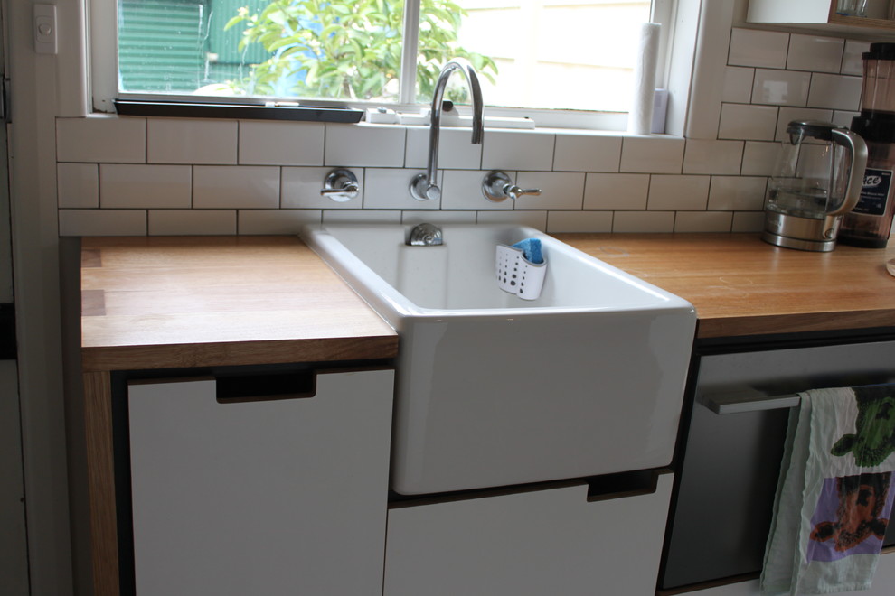 Inspiration for a small scandinavian galley separate kitchen in Melbourne with a farmhouse sink, flat-panel cabinets, white cabinets, wood benchtops, white splashback, ceramic splashback, stainless steel appliances, concrete floors and no island.