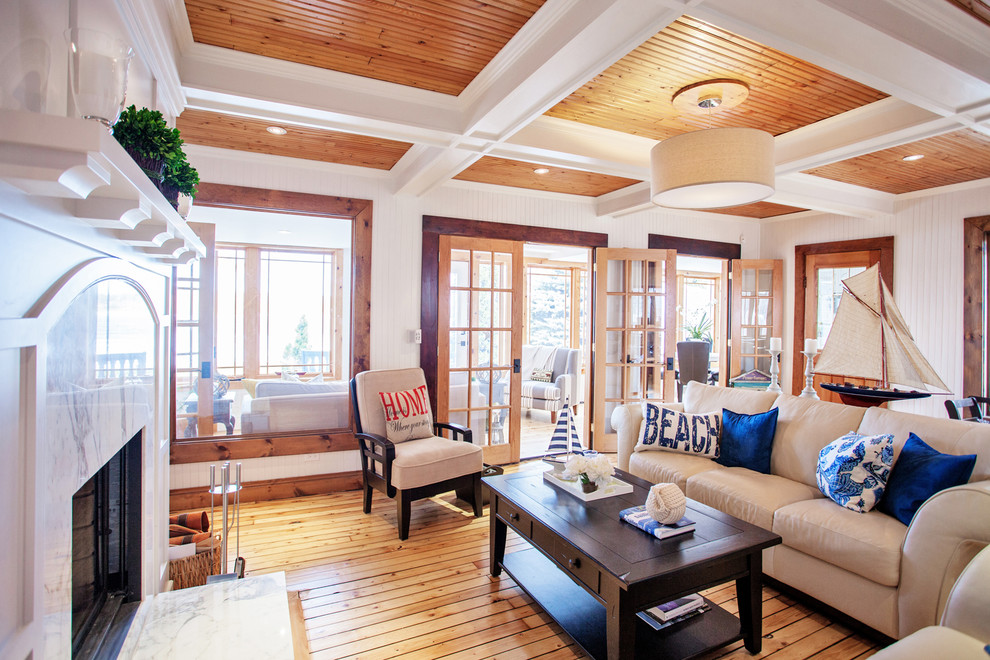 Mid-sized beach style enclosed living room in Toronto with a library, white walls, light hardwood floors, a standard fireplace, a wood fireplace surround and a built-in media wall.