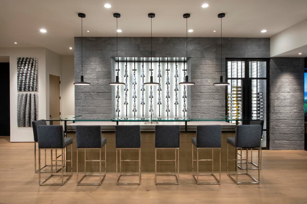 Expansive modern home bar in Phoenix with glass benchtops, grey splashback, stone tile splashback, light hardwood floors and brown floor.