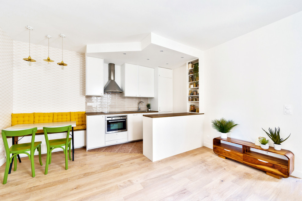 This is an example of a mid-sized modern galley open plan kitchen in Paris with an undermount sink, flat-panel cabinets, white cabinets, wood benchtops, pink splashback and terra-cotta floors.