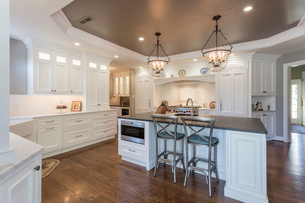 Photo of a large traditional u-shaped eat-in kitchen in Philadelphia with a farmhouse sink, recessed-panel cabinets, white cabinets, marble benchtops, white splashback, ceramic splashback, panelled appliances, dark hardwood floors and with island.