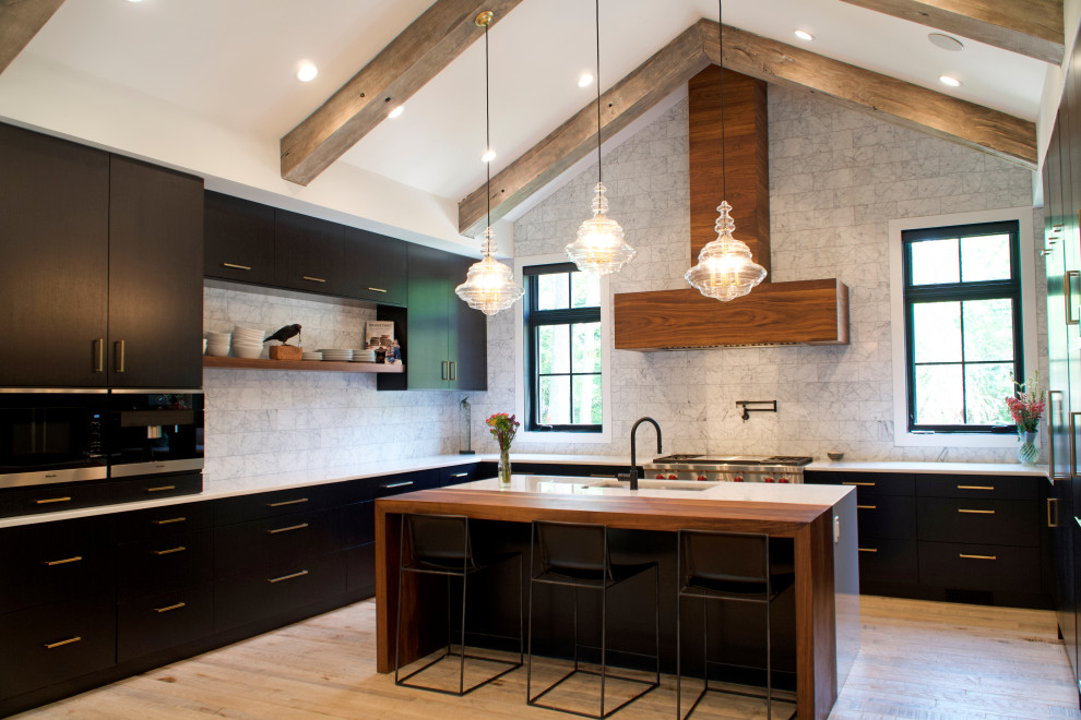 Foto på ett stort lantligt vit kök, med en undermonterad diskho, släta luckor, svarta skåp, bänkskiva i kvartsit, vitt stänkskydd, stänkskydd i stenkakel, svarta vitvaror, mellanmörkt trägolv, en köksö och beiget golv