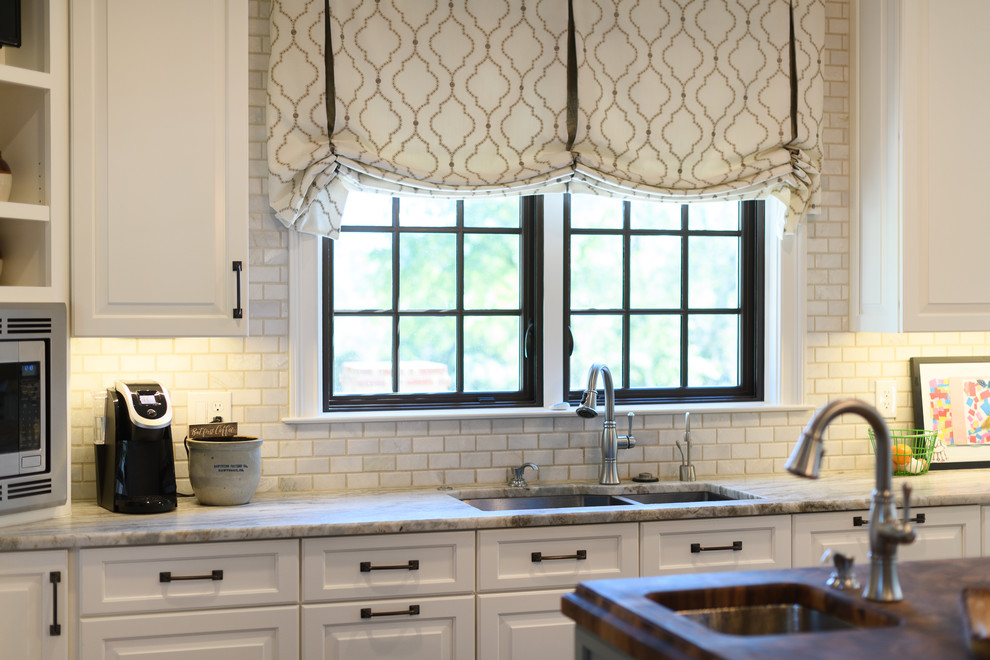 Example of a large transitional l-shaped dark wood floor and brown floor kitchen design with an undermount sink, raised-panel cabinets, white cabinets, quartzite countertops, white backsplash, marble backsplash, stainless steel appliances and an island