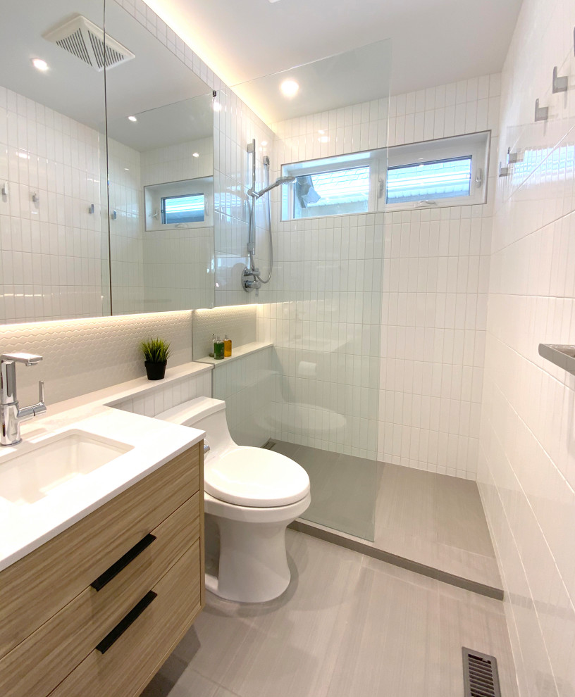 Example of a mid-sized trendy master white tile and ceramic tile porcelain tile, gray floor, single-sink and vaulted ceiling corner shower design in Calgary with flat-panel cabinets, light wood cabinets, a one-piece toilet, white walls, an undermount sink, quartz countertops, a hinged shower door, white countertops and a floating vanity