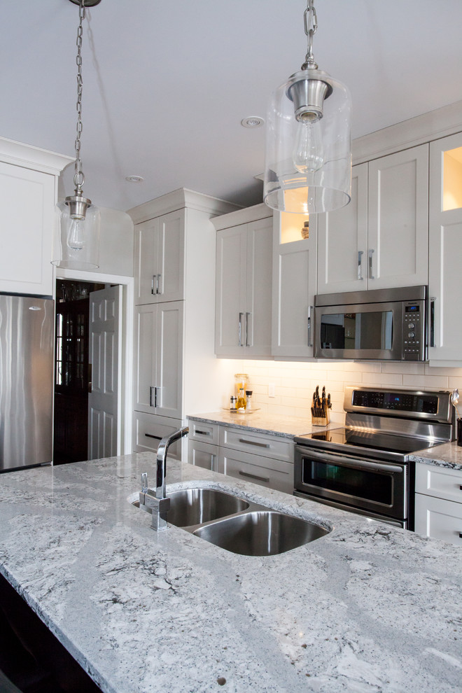 Inspiration for a large transitional u-shaped dark wood floor and brown floor eat-in kitchen remodel in Toronto with an undermount sink, shaker cabinets, white cabinets, quartz countertops, white backsplash, subway tile backsplash, stainless steel appliances, an island and white countertops