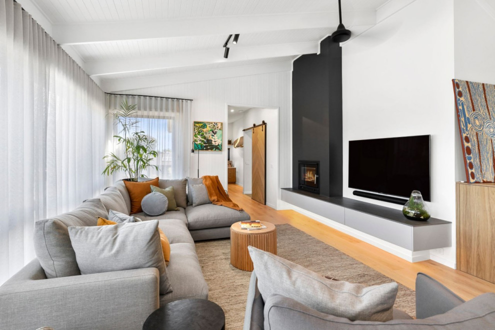 Mittelgroßes, Offenes Modernes Wohnzimmer mit weißer Wandfarbe, hellem Holzboden, Kamin, verputzter Kaminumrandung, TV-Wand und freigelegten Dachbalken in Geelong
