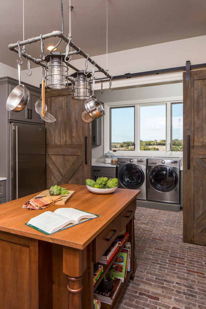 Inspiration for a large industrial l-shaped separate kitchen in Austin with an undermount sink, grey cabinets, stainless steel appliances, brick floors, with island, shaker cabinets, wood benchtops, brown splashback, brick splashback and brown floor.