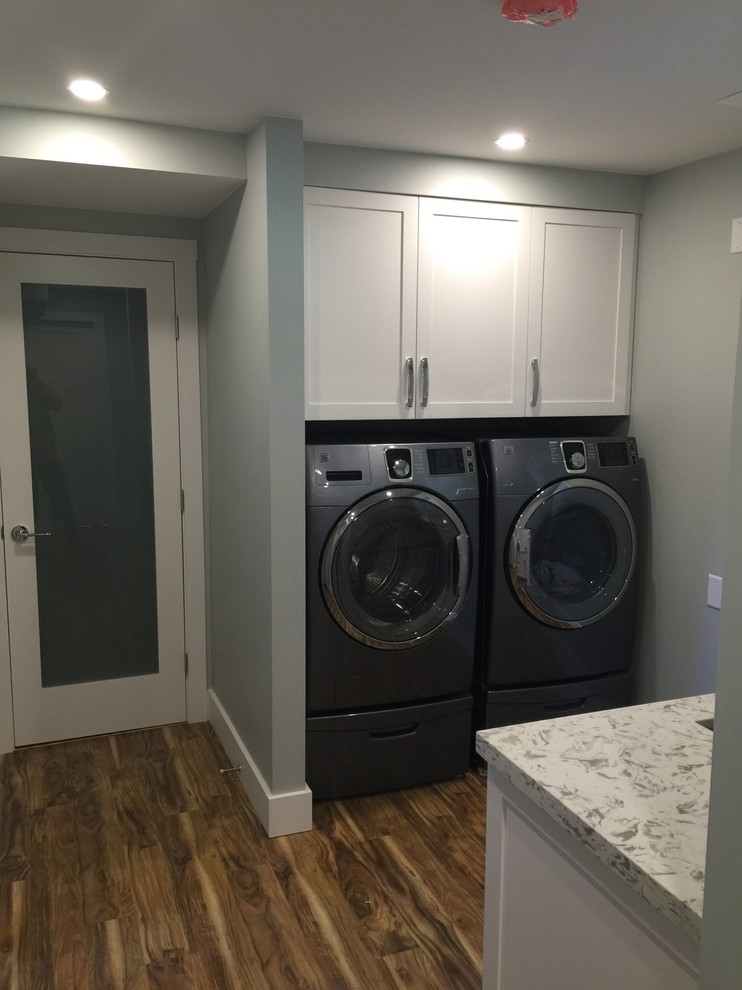 Contemporary galley dedicated laundry room in Vancouver with an undermount sink, shaker cabinets, white cabinets, quartz benchtops, medium hardwood floors and a side-by-side washer and dryer.