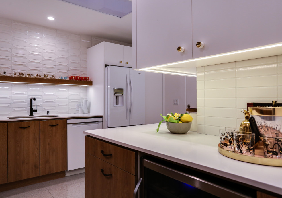 Photo of a mid-sized midcentury l-shaped kitchen in Other with an undermount sink, flat-panel cabinets, white cabinets, quartz benchtops, white splashback, ceramic splashback, white appliances, ceramic floors, a peninsula, grey floor and white benchtop.