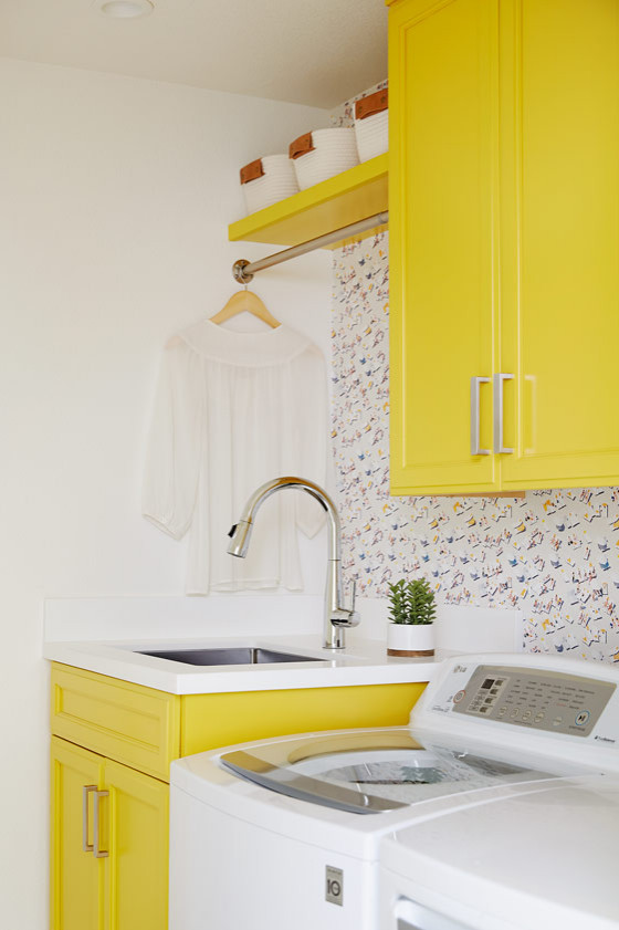 Modelo de cuarto de lavado actual de tamaño medio con fregadero bajoencimera, armarios estilo shaker, puertas de armario amarillas, paredes blancas y lavadora y secadora juntas