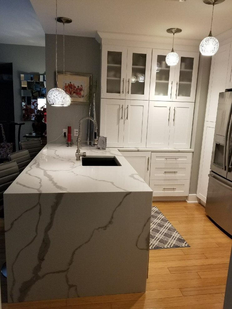 Photo of a mid-sized contemporary u-shaped eat-in kitchen in Tampa with an undermount sink, shaker cabinets, white cabinets, quartz benchtops, white splashback, subway tile splashback, stainless steel appliances, light hardwood floors, a peninsula, yellow floor and white benchtop.