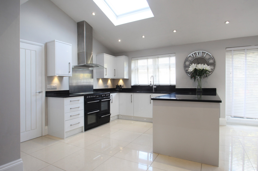 Photo of a medium sized modern l-shaped open plan kitchen in Cheshire with a double-bowl sink, flat-panel cabinets, white cabinets, granite worktops, metallic splashback, metal splashback, black appliances, porcelain flooring, a breakfast bar, beige floors and black worktops.