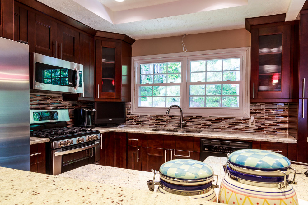 Photo of a small transitional l-shaped separate kitchen in Atlanta with a double-bowl sink, recessed-panel cabinets, dark wood cabinets, granite benchtops, multi-coloured splashback, matchstick tile splashback, stainless steel appliances, travertine floors, no island and beige floor.