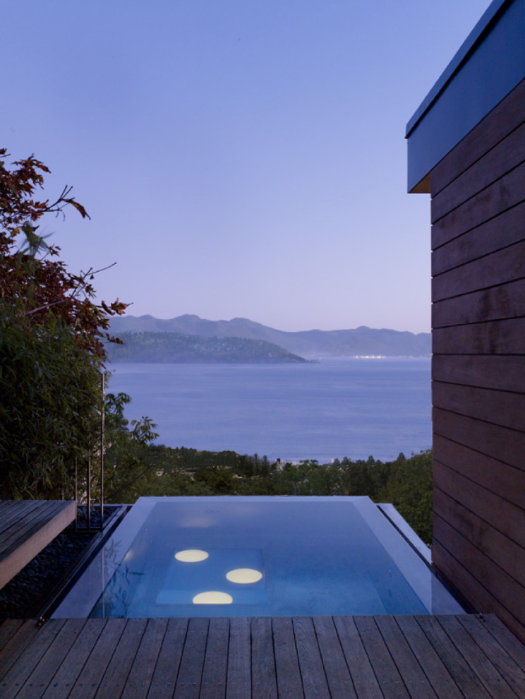This is an example of a modern side yard rectangular infinity pool in San Francisco with with privacy feature and decking.