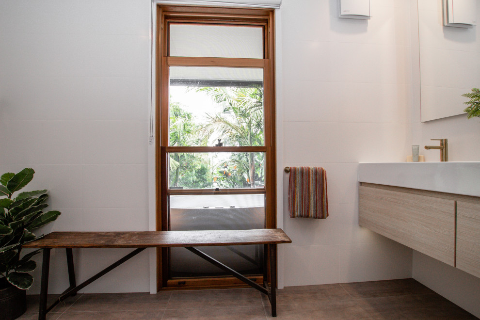 Inspiration for a mid-sized mediterranean 3/4 bathroom in Sydney with flat-panel cabinets, light wood cabinets, a freestanding tub, a corner shower, a two-piece toilet, an integrated sink, a hinged shower door, white benchtops, a niche, a double vanity and a floating vanity.
