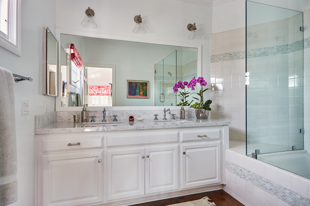 Mid-sized transitional kids bathroom in Orange County with white cabinets, white tile, white walls, an undermount sink, marble benchtops, raised-panel cabinets, a drop-in tub, a shower/bathtub combo, porcelain tile and medium hardwood floors.