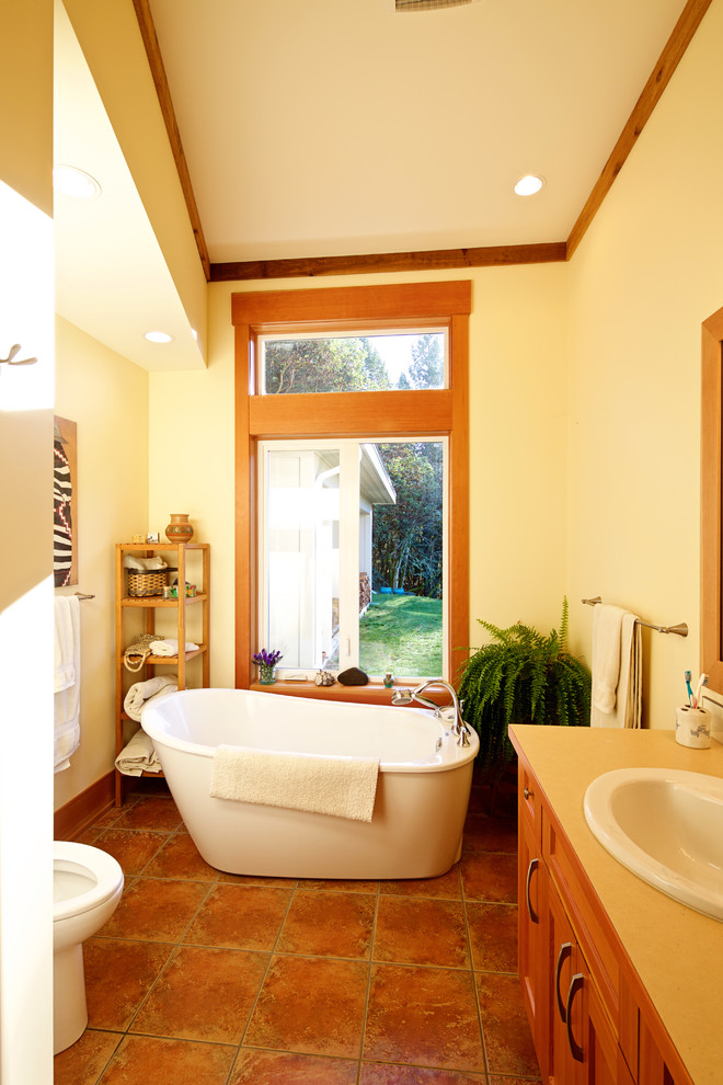 Inspiration for a mid-sized country master bathroom in Vancouver with a drop-in sink, shaker cabinets, medium wood cabinets, solid surface benchtops, a freestanding tub, an open shower, a one-piece toilet, multi-coloured tile, terra-cotta tile, white walls and terra-cotta floors.