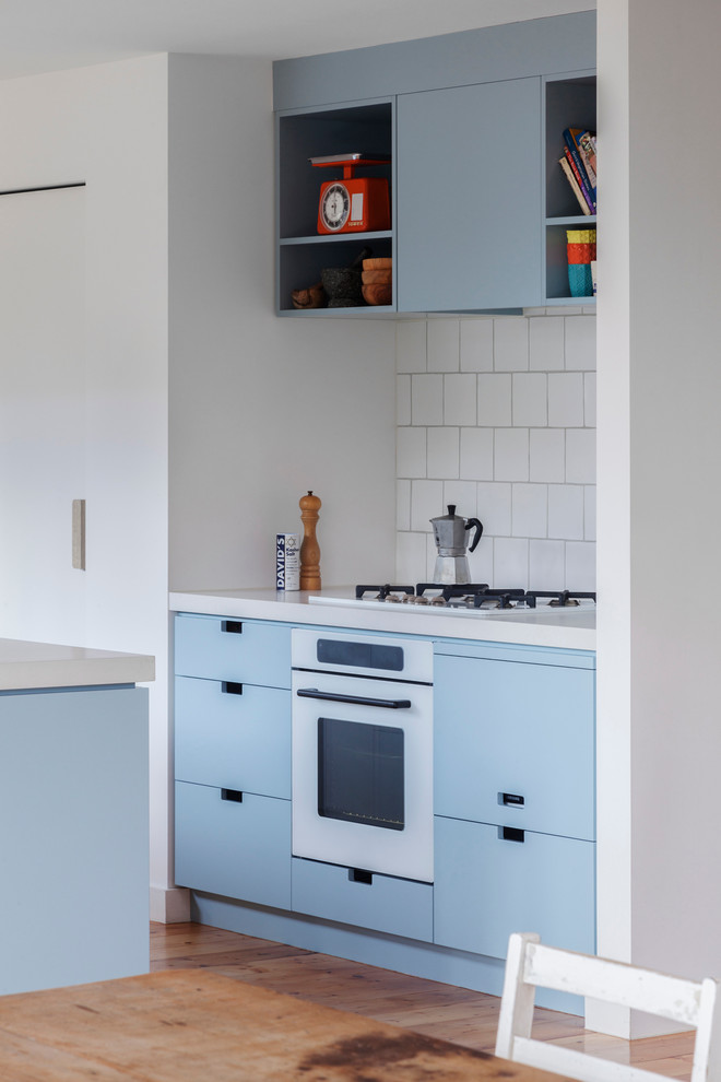 Design ideas for a mid-sized contemporary galley kitchen in Melbourne with a double-bowl sink, blue cabinets, quartz benchtops, white splashback, ceramic splashback, white appliances, light hardwood floors and no island.