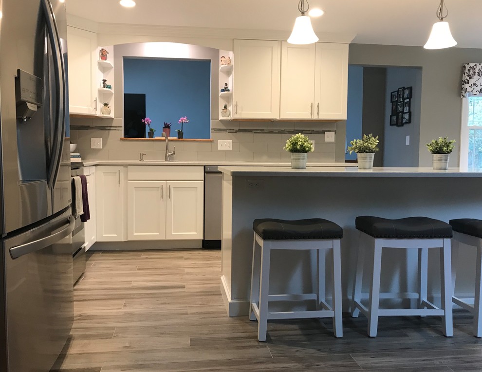 Example of a mid-sized transitional l-shaped porcelain tile and gray floor open concept kitchen design in Boston with a single-bowl sink, flat-panel cabinets, white cabinets, quartz countertops, gray backsplash, subway tile backsplash, stainless steel appliances, an island and white countertops