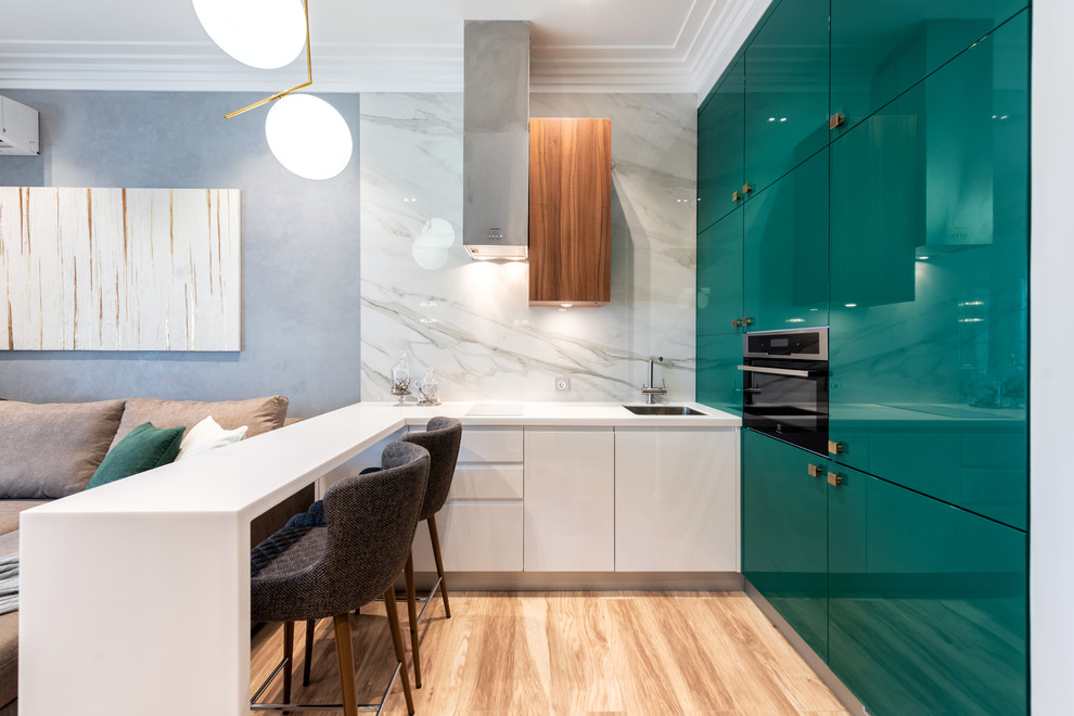 Photo of a contemporary l-shaped open plan kitchen in Other with a single-bowl sink, flat-panel cabinets, solid surface benchtops, white splashback, white benchtop, turquoise cabinets, stone slab splashback, black appliances, light hardwood floors, a peninsula and beige floor.